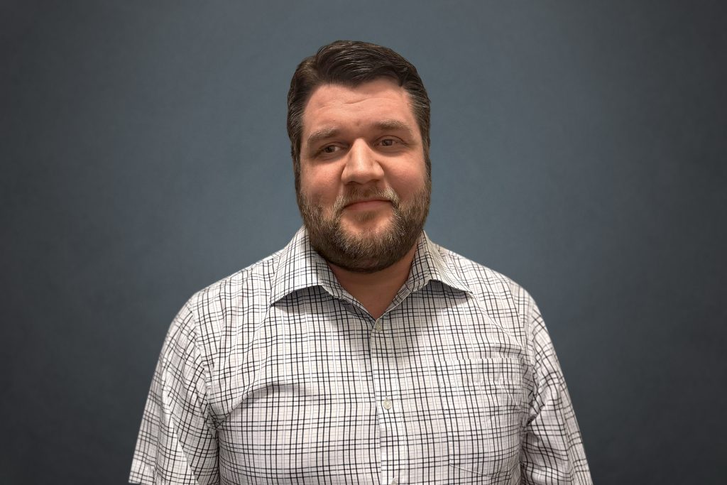 Headshot of Justin Byram wearing checkered shirt